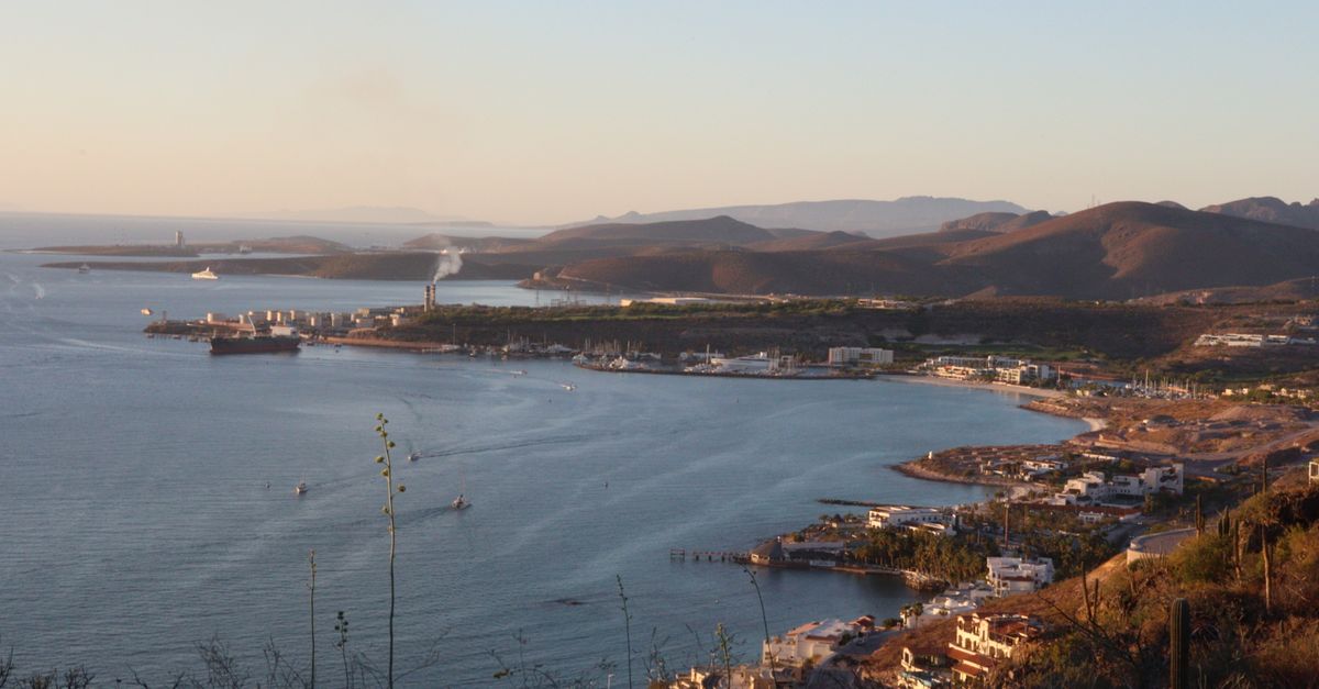 Scenic aerial view of a coastal port city with mountains, at sunrise, capturing serene waters and surrounding landscape.